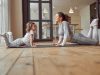 Low angle of cheerful woman doing exercises together with cute girl on floor for improving flexibility
